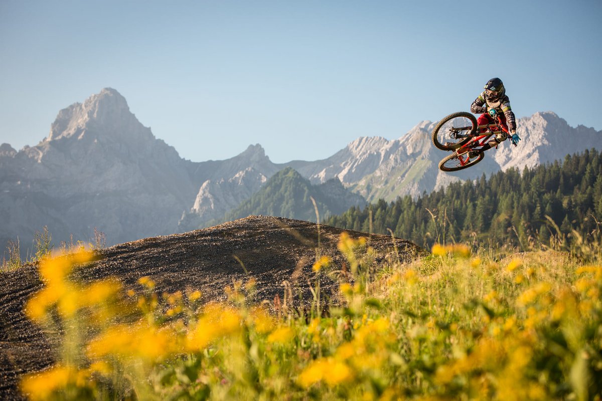 Mountainbiker mit neongrünem Helm macht einen Whip-Sprung auf dem Dirt-Trail des Bikeparks Brandnertal