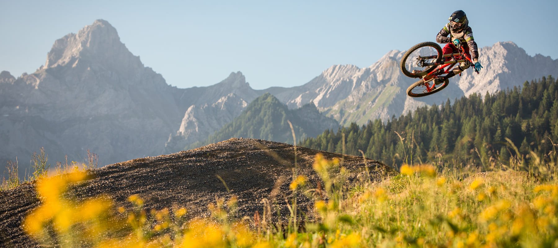 Mountainbiker mit neongrünem Helm macht einen Whip-Sprung auf dem Dirt-Trail des Bikeparks Brandnertal