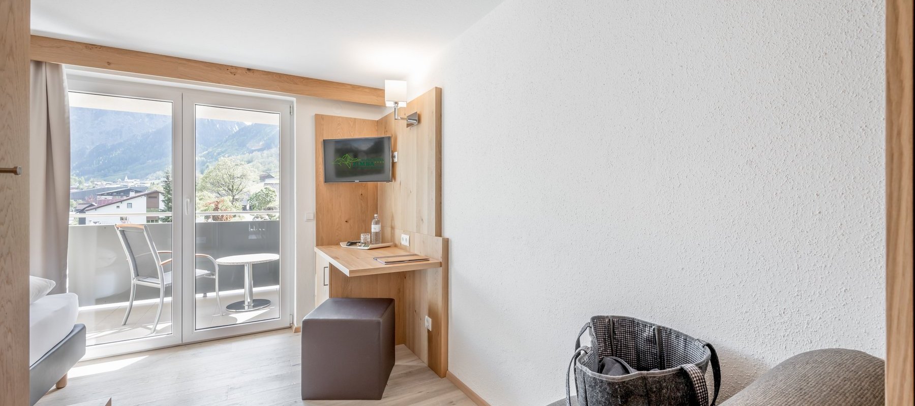 Zimmer mit Bett, Balkon, Lesesessel und Schreibtisch mit TV