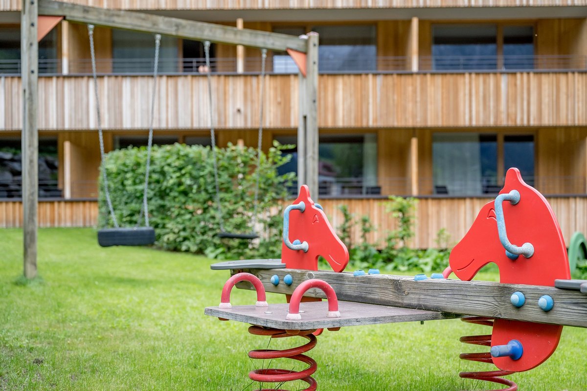 Kinderwippe mit roten Pferdeköpfen und Schaukelgestell mit Reifen in einem Garten 