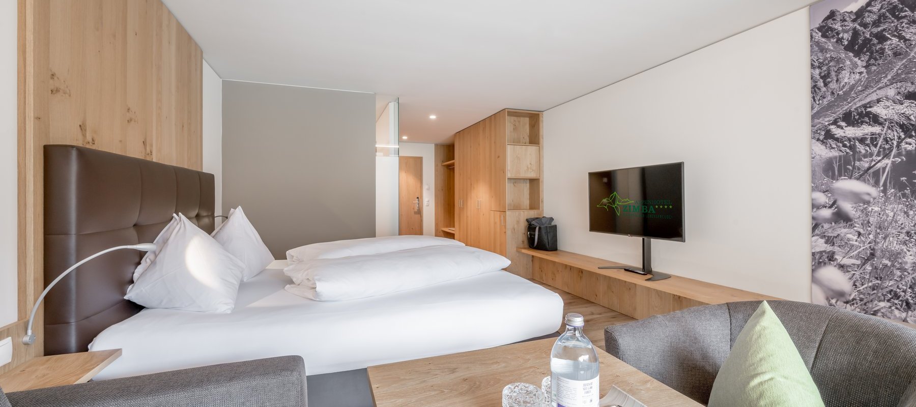 Modernes Hotelzimmer mit Parkettboden, gemütlichem Doppelbett, Sitzbereich und Fernseher