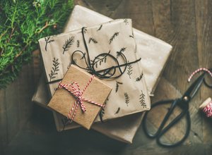 Nachhaltig verpackte Geschenke mit Naturmotiven und Bast auf Holztisch mit Tannenzweigen