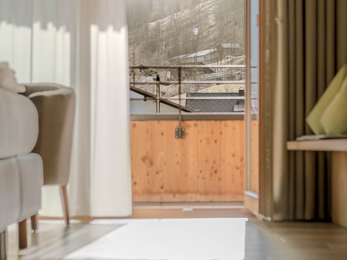 Blick aus einem hellen Zimmer durch offene Türen auf einen Balkon und die umliegende Landschaft