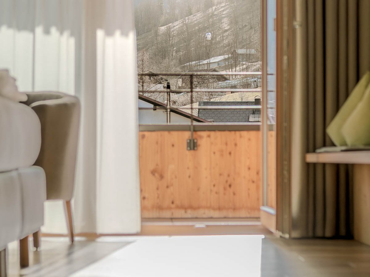 Blick aus einem hellen Zimmer durch offene Türen auf einen Balkon und die umliegende Landschaft
