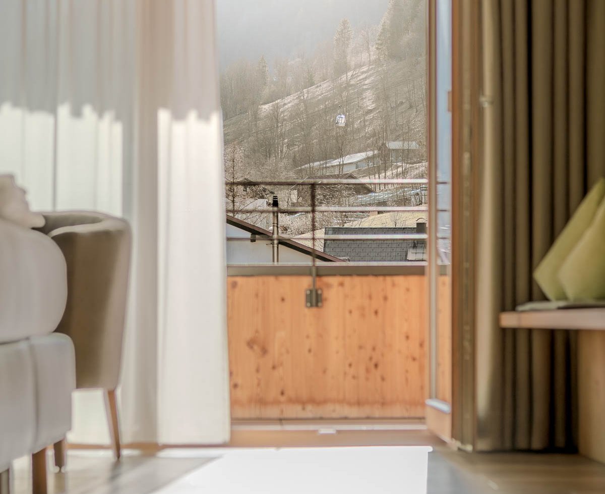 Blick aus einem hellen Zimmer durch offene Türen auf einen Balkon und die umliegende Landschaft
