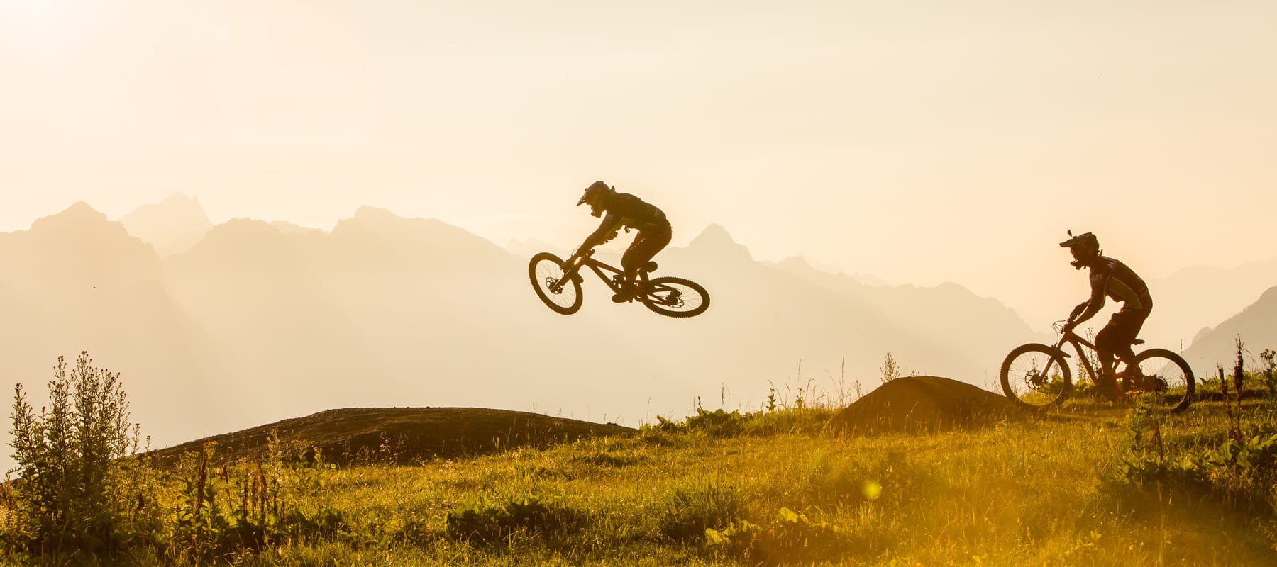 Zwei Mountainbiker als Silhouetten im Gegenlicht bei Sonnenuntergang mit Bergpanorama im Hintergrund