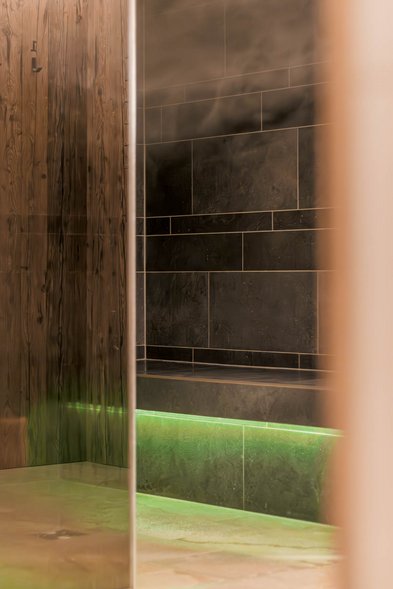 Dampfbad mit dunklen Fliesen und indirekter Beleuchtung