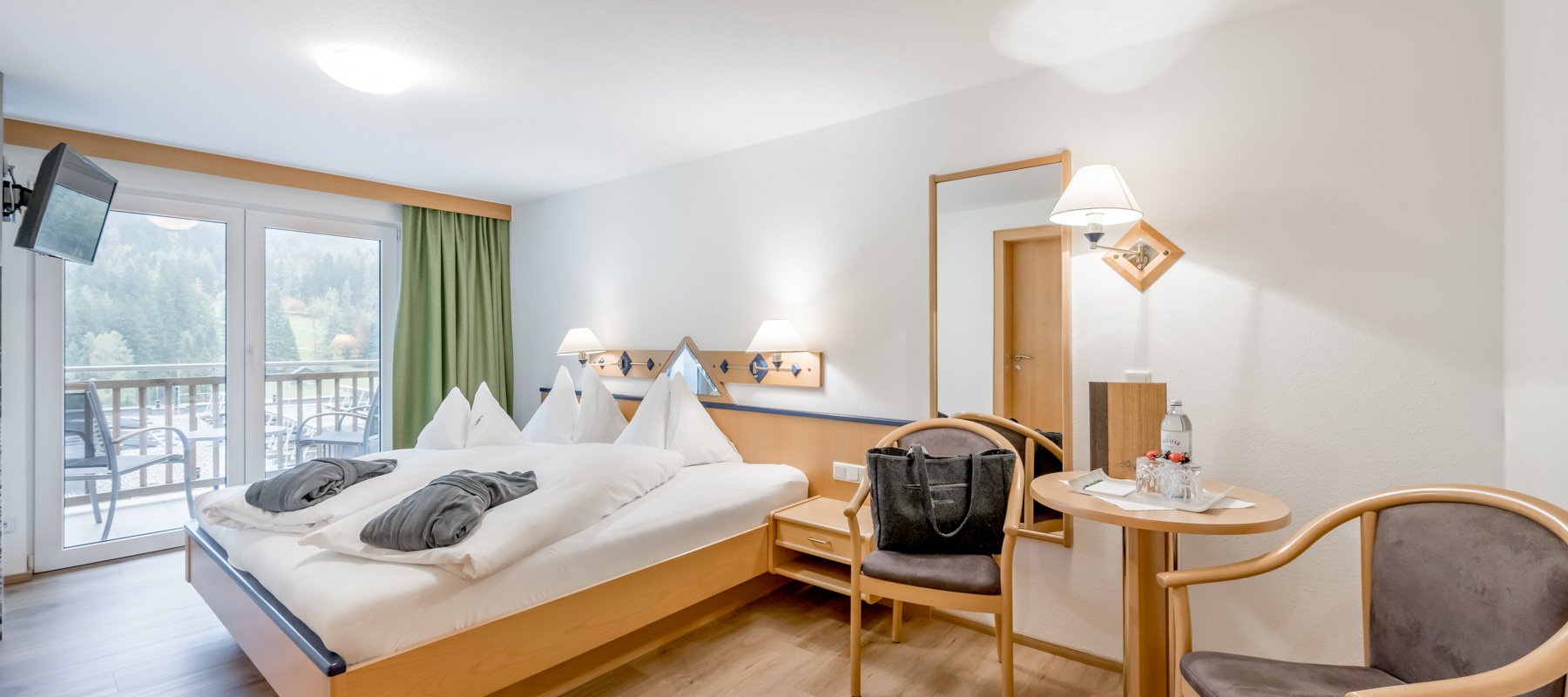 Hotelzimmer mit Doppelbett, Sitzecke, TV und Balkon mit Waldblick