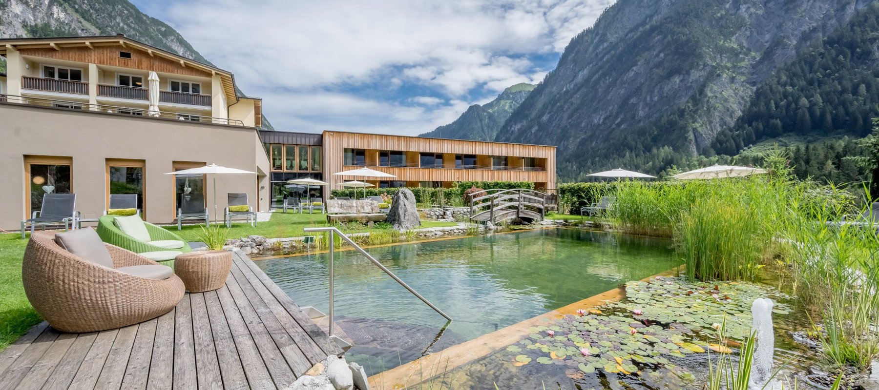 Hotel mit Naturbadeteich und gemütlichen Gartenmöbeln in den Bergen im Sommer