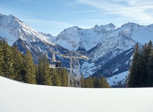 Seilbahn fährt durch verschneite Winterlandschaft mit Blick auf die Alpen und Wälder