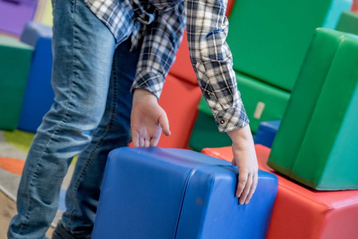 Kind spielt mit gepolsterten Würfeln zum Stapeln in einem Spielzimmer