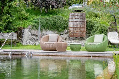 Badeteich in einem sonnigen Garten in mit gemütlichen Sitzschalen und Gartendusche