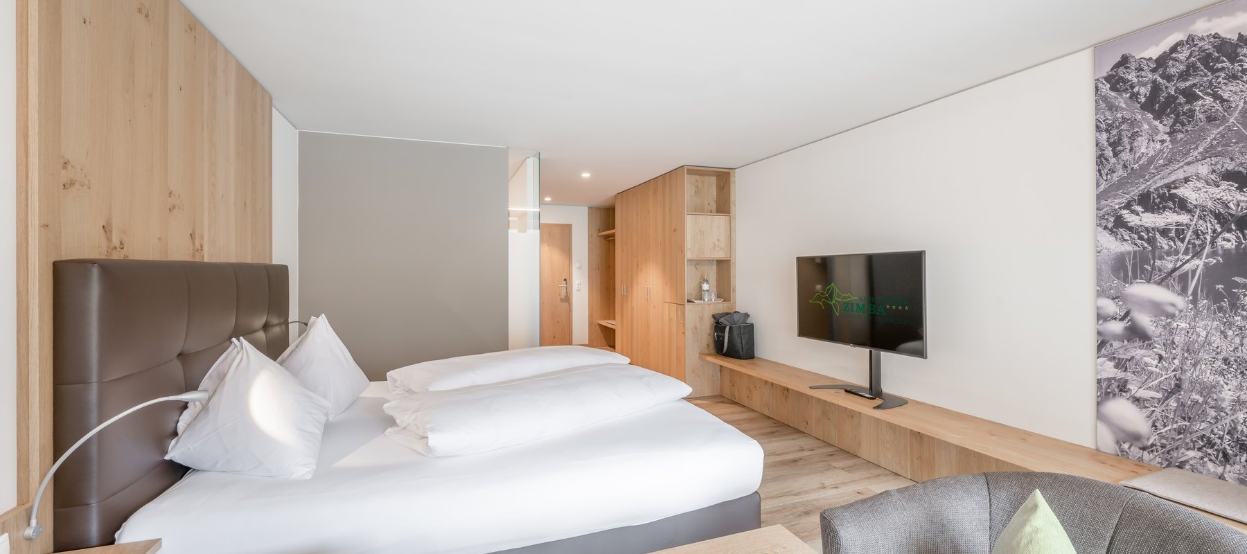 Modernes Hotelzimmer mit Parkettboden, gemütlichem Doppelbett, Sitzbereich und Fernseher