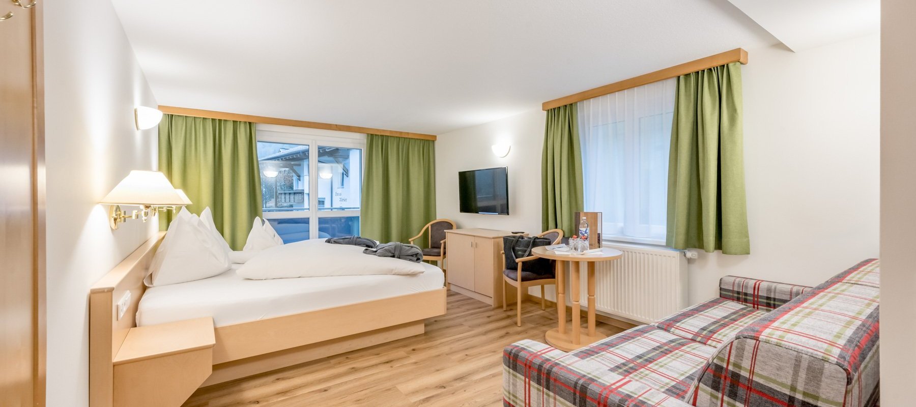 Hotelzimmer mit großem Sofa, Schreibtisch mit TV und und Balkon