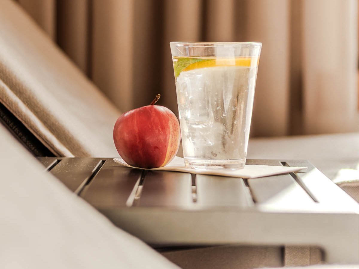 Erfrischungsgetränk mit Zitronenscheibe und Apfel auf einem Beistelltisch neben einer Liege