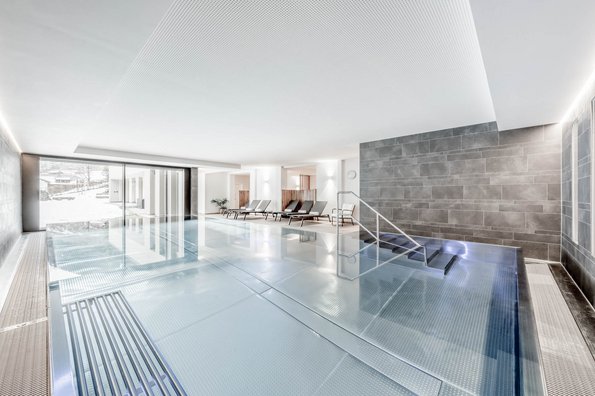 Indoor-Infinity-Pool in einem hellen Raum mit großen Fenstern und Liegebereich