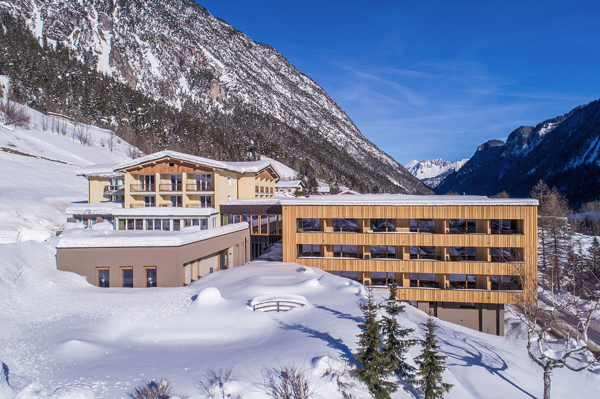 Hotel mit verschneitem Garten in den Bergen im Winter bei Sonnenschein